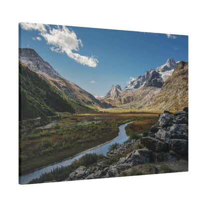 Snow-capped mountains flank a winding river through a grassy valley, with a rocky foreground under a blue sky.