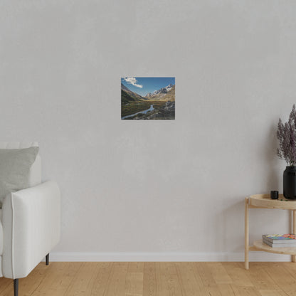 Small landscape painting of mountains, river, and blue sky hung centered on a light gray wall.