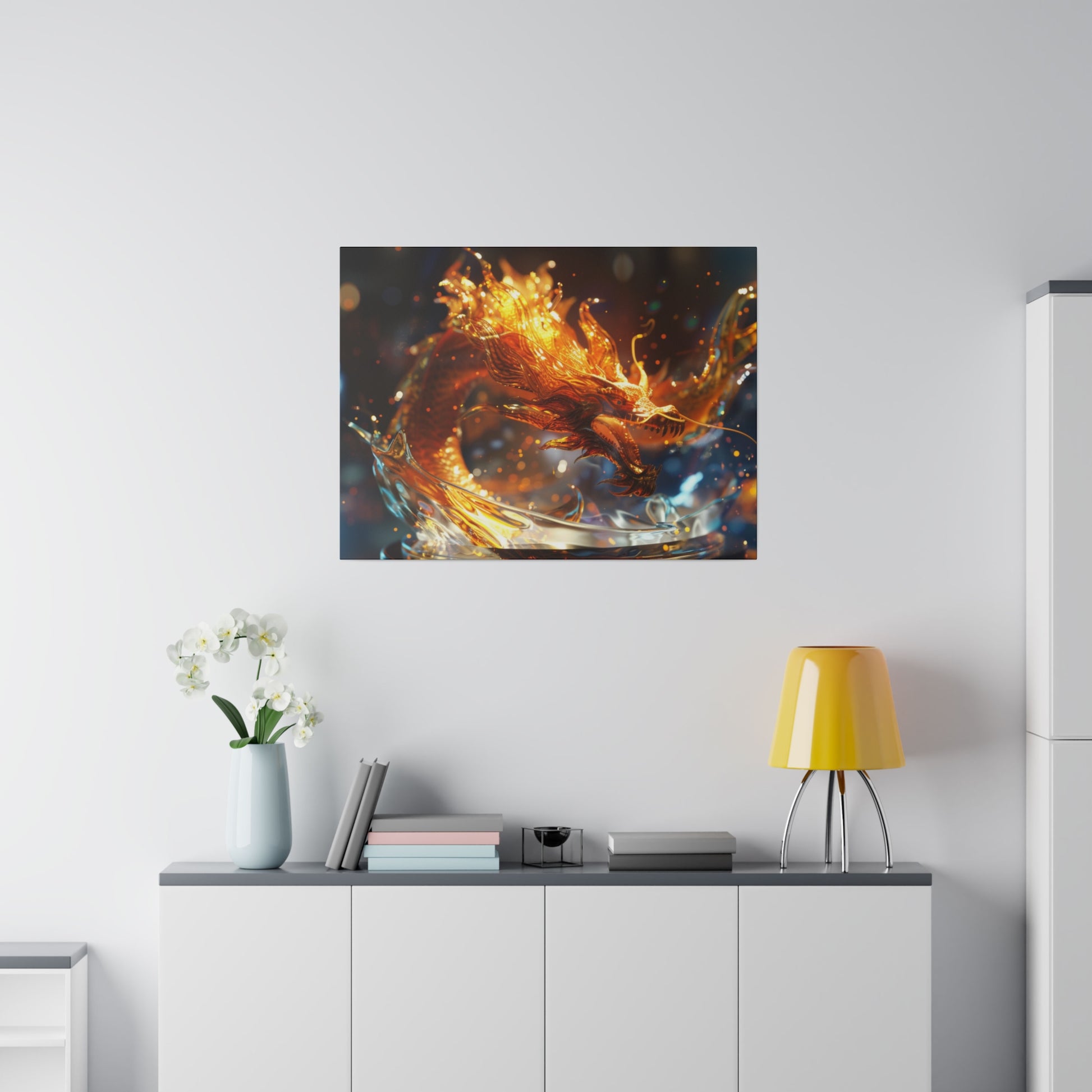 Framed abstract artwork of a fiery dragon in orange and blue hues hangs above a white cabinet with a yellow lamp and vase of white flowers.