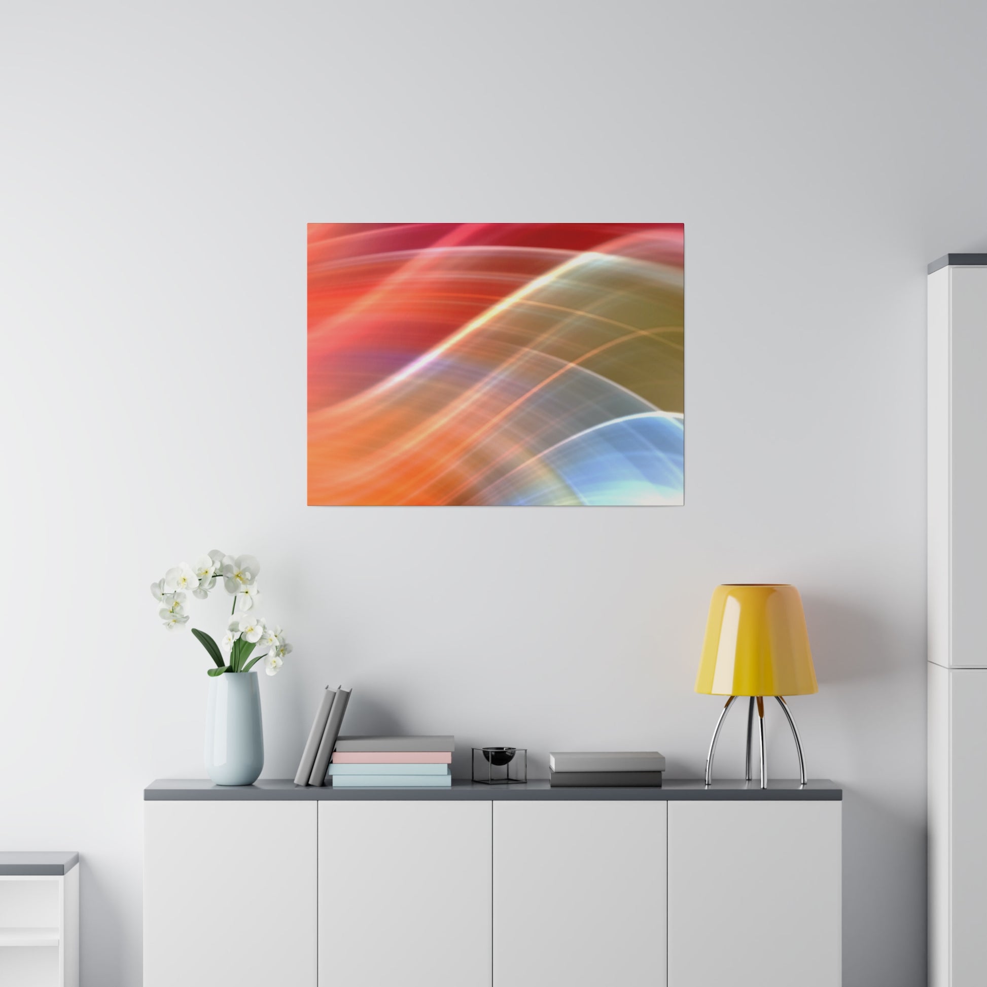 Abstract colorful wall art with orange, red, and blue curves hangs above a white cabinet with a blue vase of white flowers, books, and a