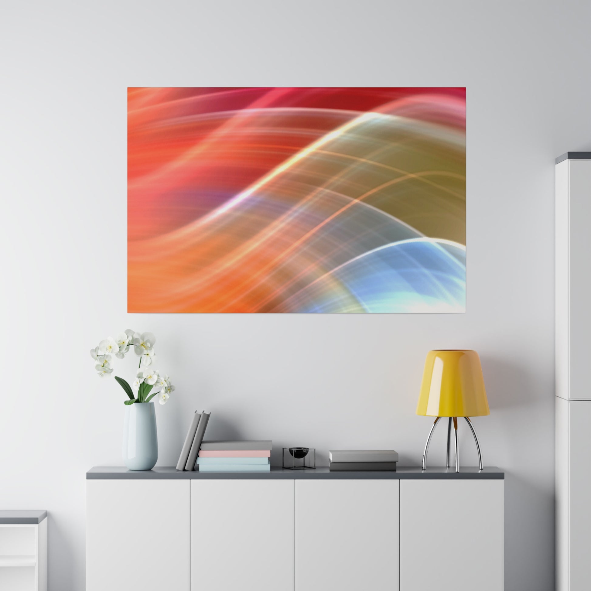 Abstract colorful swirl print on a white wall above a cabinet with a pale blue vase of white flowers, books, and a yellow lamp.