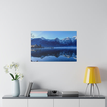 Framed blue-toned landscape photo of snow-capped mountains reflected in a calm lake, with a small village on the left.