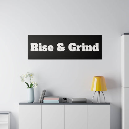 Black rectangular wall sign with bold white text "Rise & Grind" above a white cabinet with a yellow lamp.