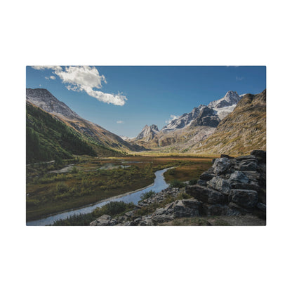 Mountain valley with a winding river, green slopes, and a rocky foreground under a bright blue sky.