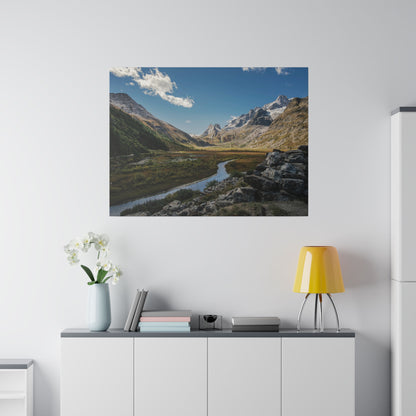 Mounted landscape photo of a mountain valley with a winding river, rocky foreground, and snow-capped peaks under a blue sky.