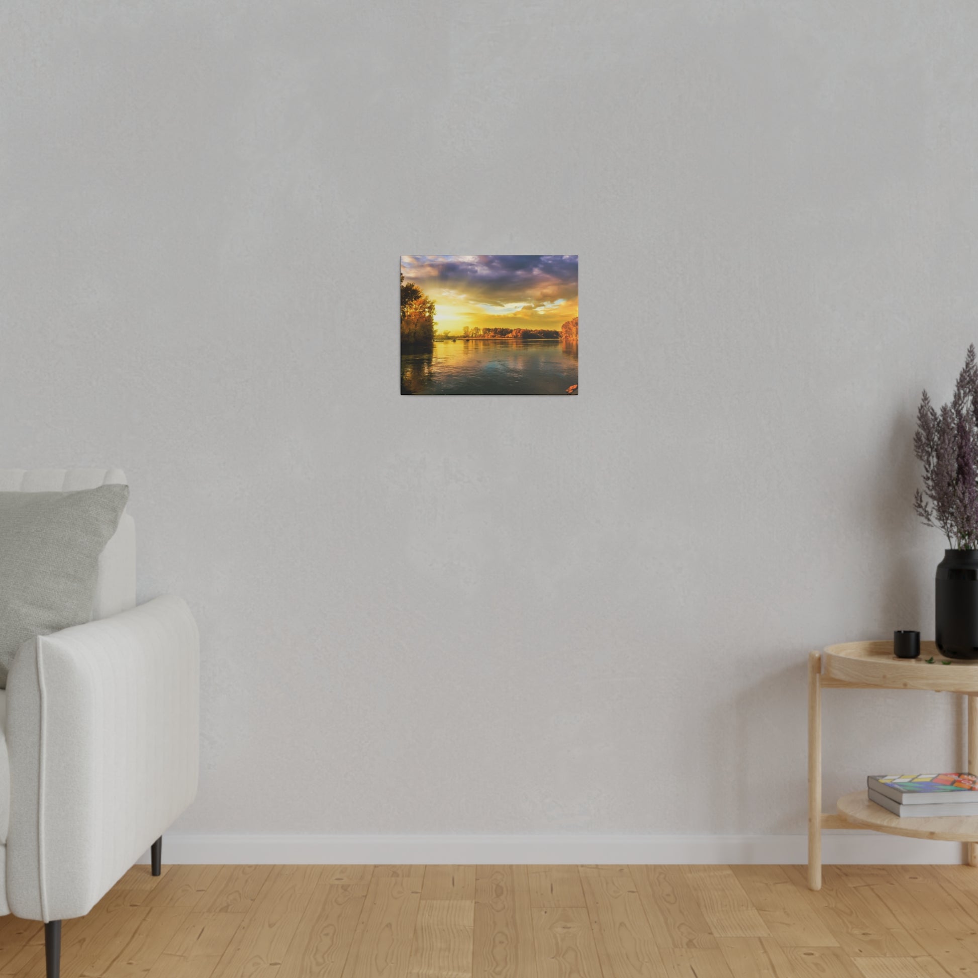 Small square painting of a sunset over a river hung on a light gray wall, with a white sofa to the left and a wooden side table on the