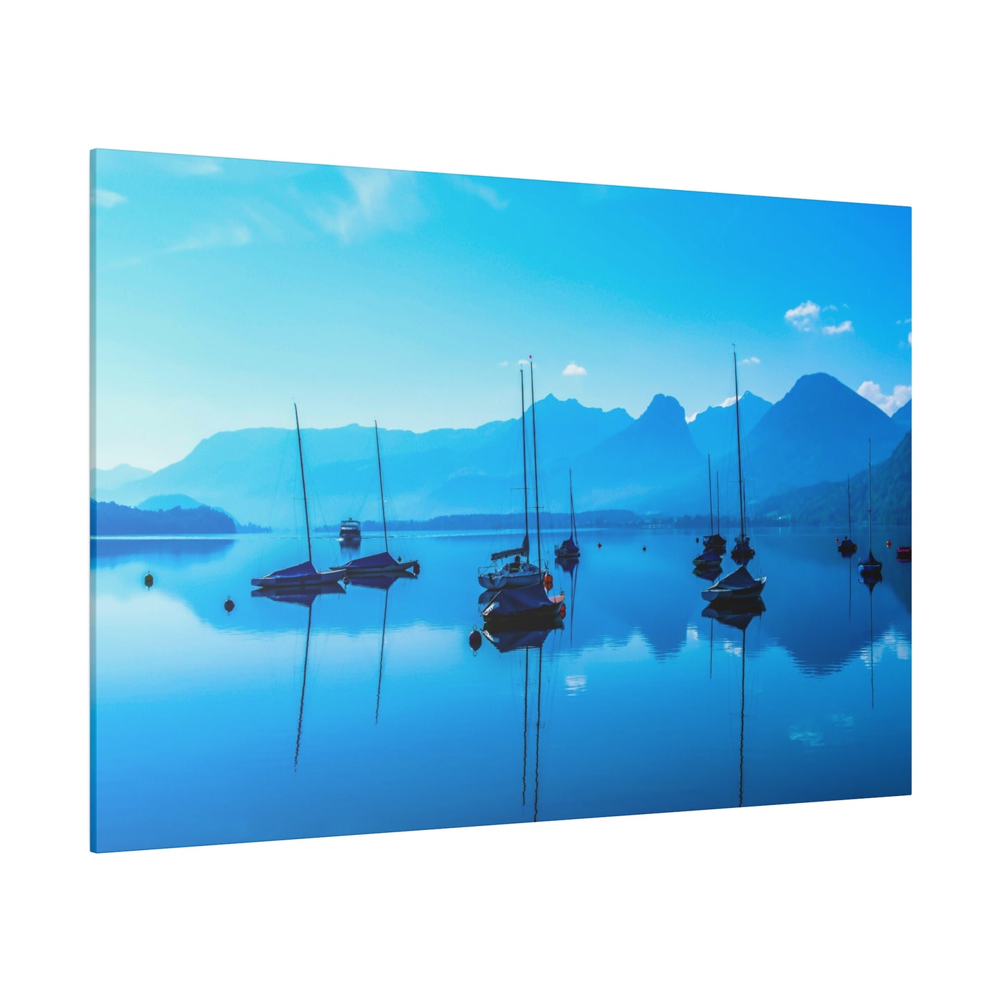 Sailboats anchored on a calm lake, reflecting the clear blue sky. The mountains in the background enhance the serene and peaceful atmosphere of the scene.