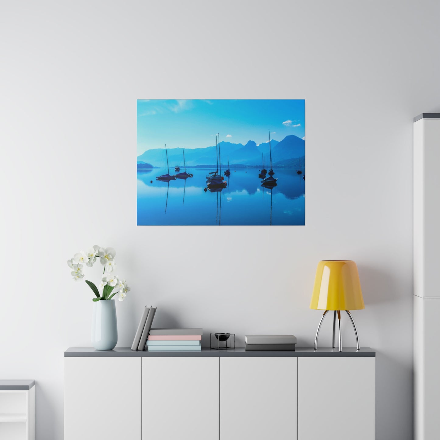 Sailboats anchored on a tranquil blue lake, reflecting the clear sky and surrounded by mountains. The serene scene captures a peaceful and calm atmosphere.