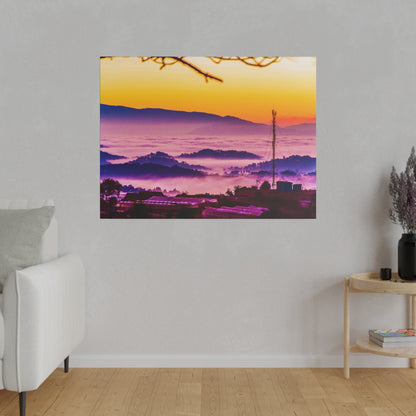 Colorful landscape photograph of a sunrise over misty hills with purple and orange tones, mounted on a gray wall.