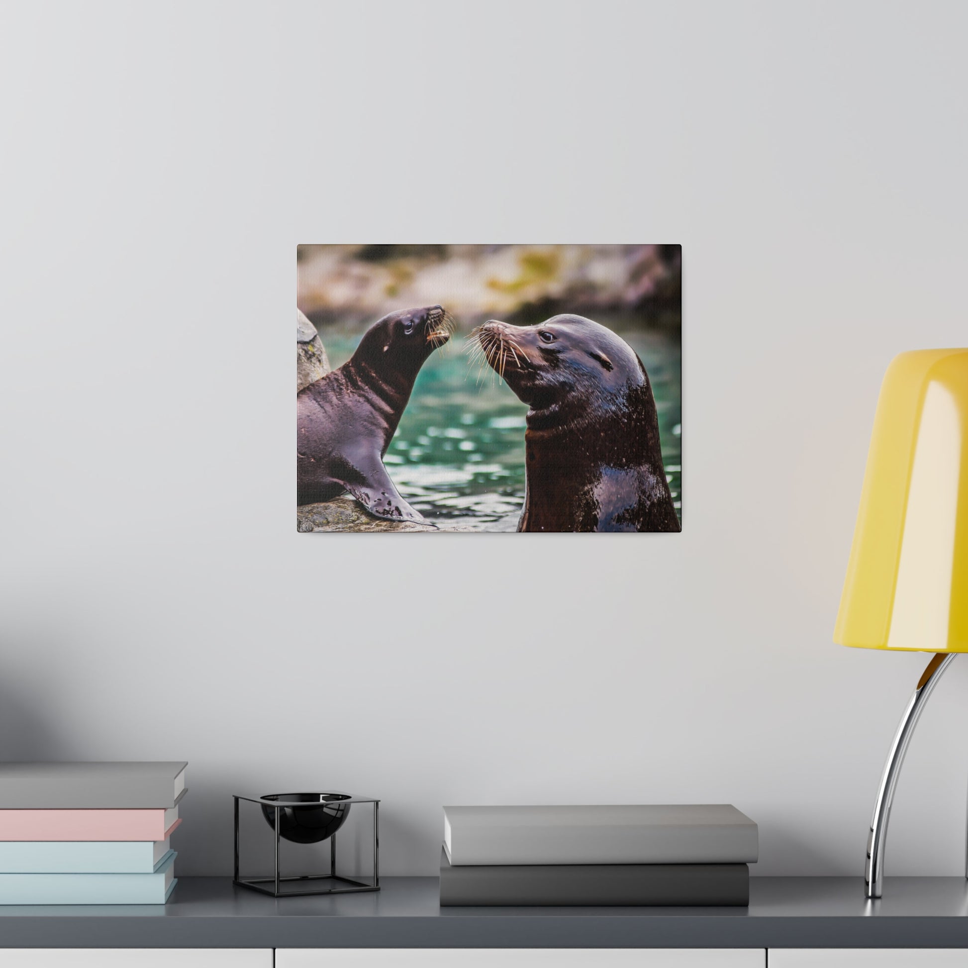 Two sea lions touching whiskers in a playful interaction by the water. Their smooth fur and curious expressions capture their social nature.