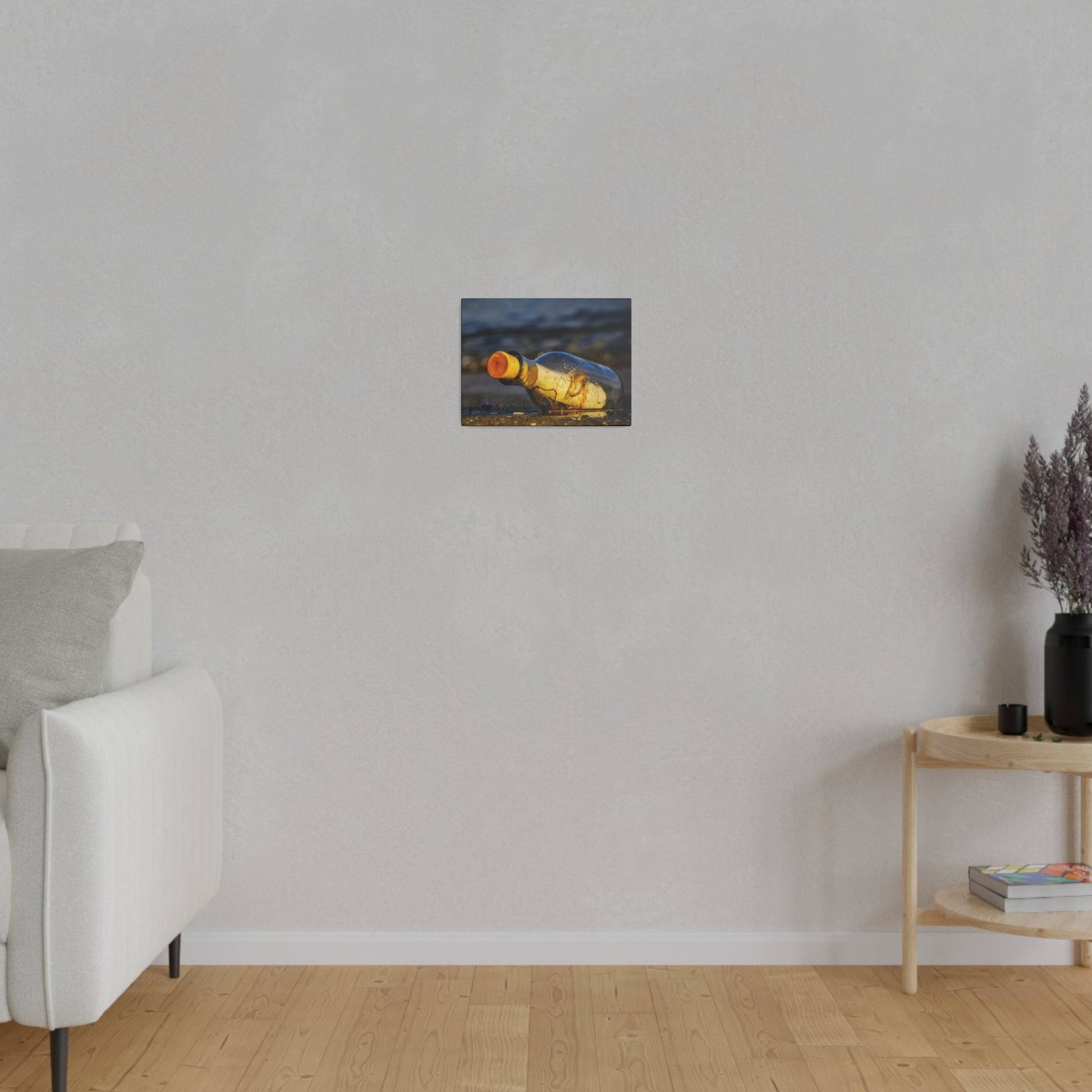 Small rectangular painting of a yellow-brown bottle lying on a shore, hung on a light gray living room wall.