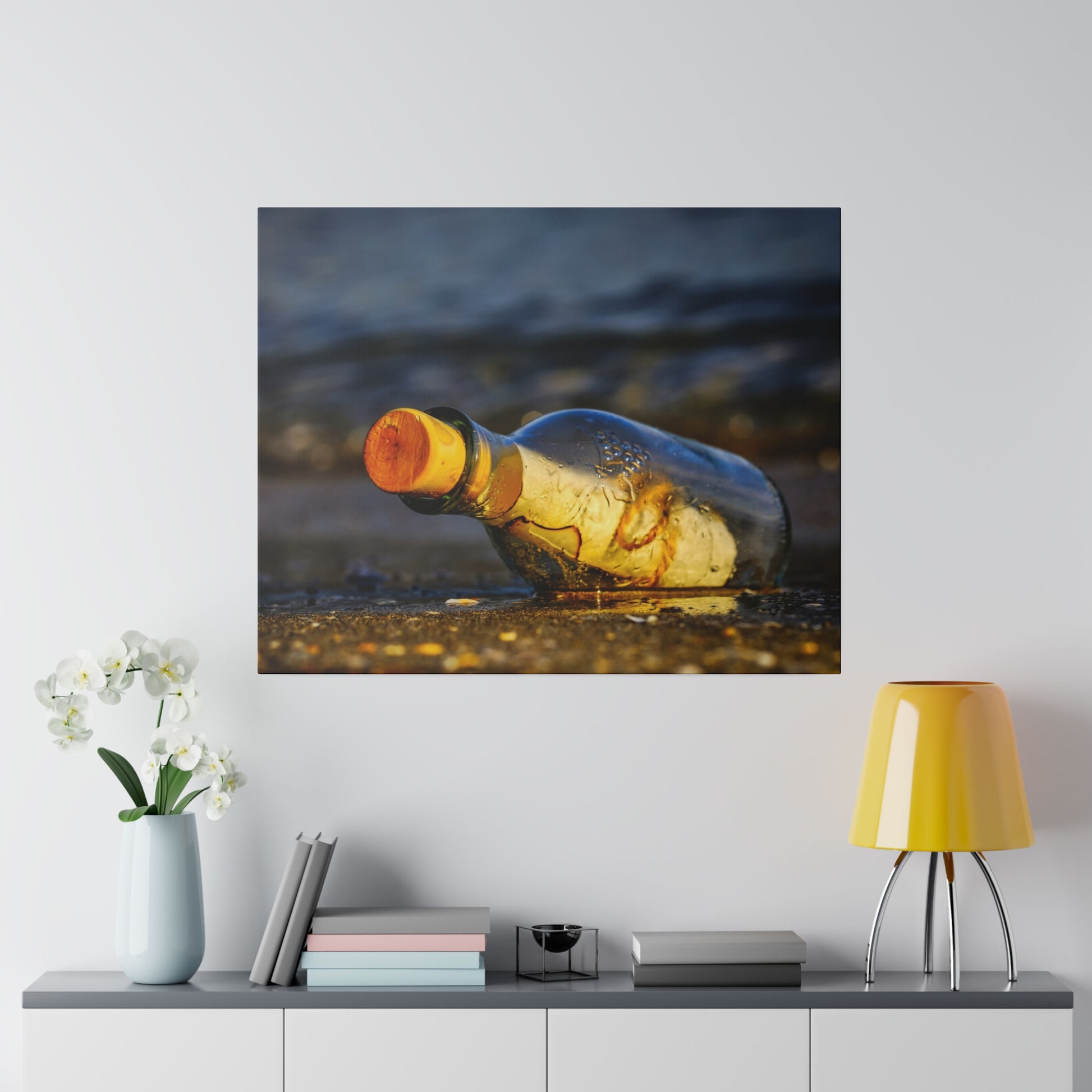 A wet, empty glass bottle with an orange cap lies on a sandy beach.
