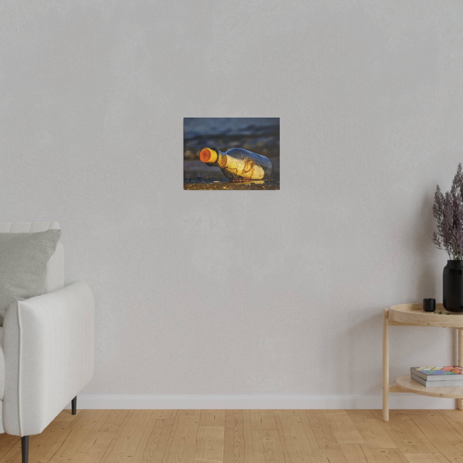 Small rectangular painting of a yellow bottle lying on a beach, hung on a light gray living room wall.