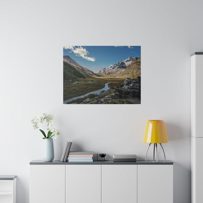 Photo of a mountain valley with a winding river, snow‑capped peaks and blue sky, hung above a white cabinet with a yellow lamp and white