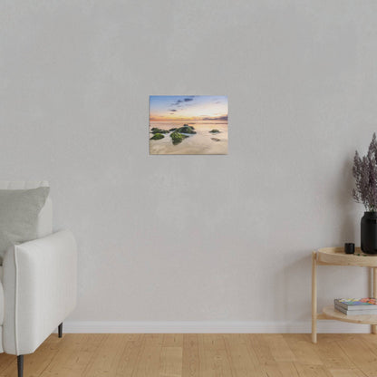 Small square landscape painting of mossy rocks in calm water at sunset, mounted on a light gray wall.