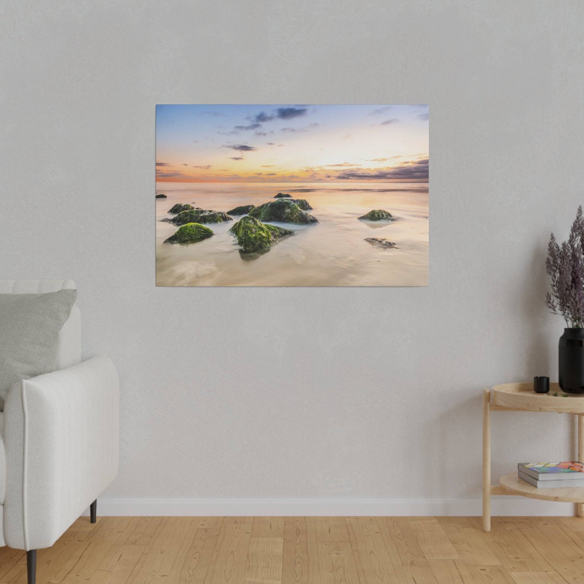 Wall-mounted canvas showing a sunset over calm water with mossy rocks in the foreground.