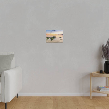Small landscape painting of a beach scene with rocks, mounted on a light gray wall above a white sofa.