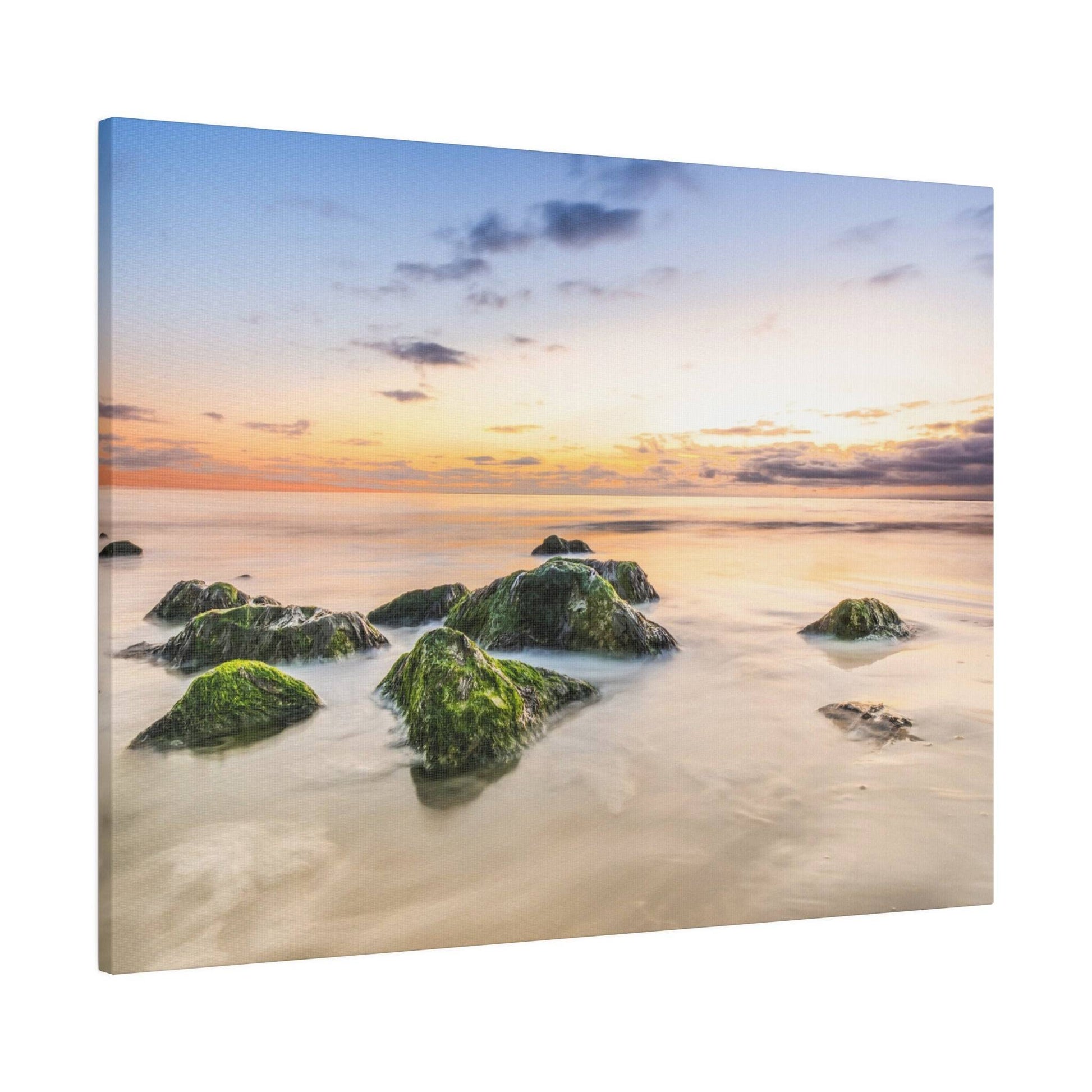 Group of moss-covered rocks in shallow coastal water at sunset with an orange and blue sky.
