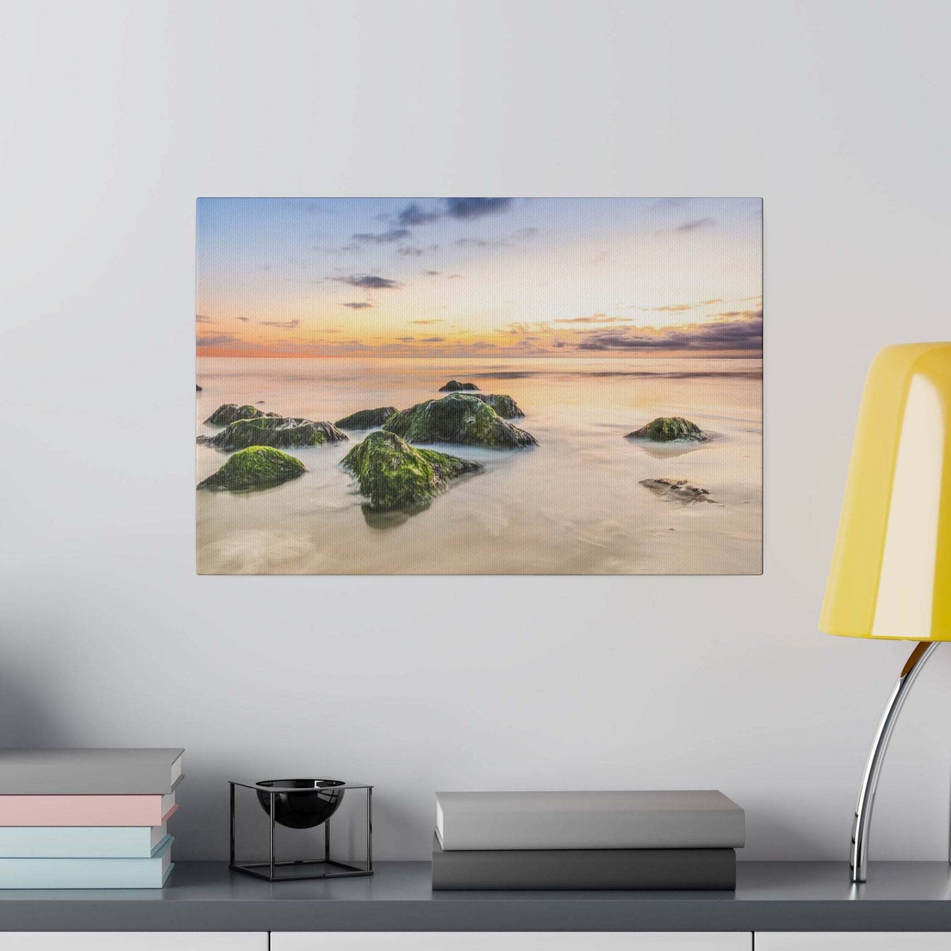 Painting of a sunset over a calm beach with moss-covered rocks in shallow water.