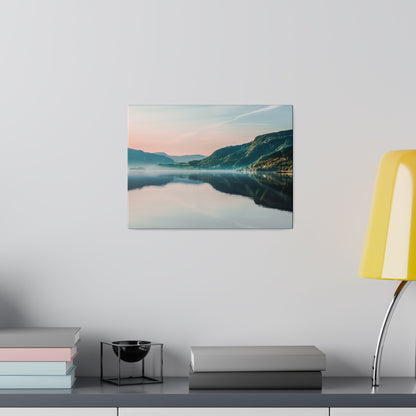 Landscape photograph print of a calm lake and mountains mounted on a light gray wall above a desk with books and a yellow lamp.