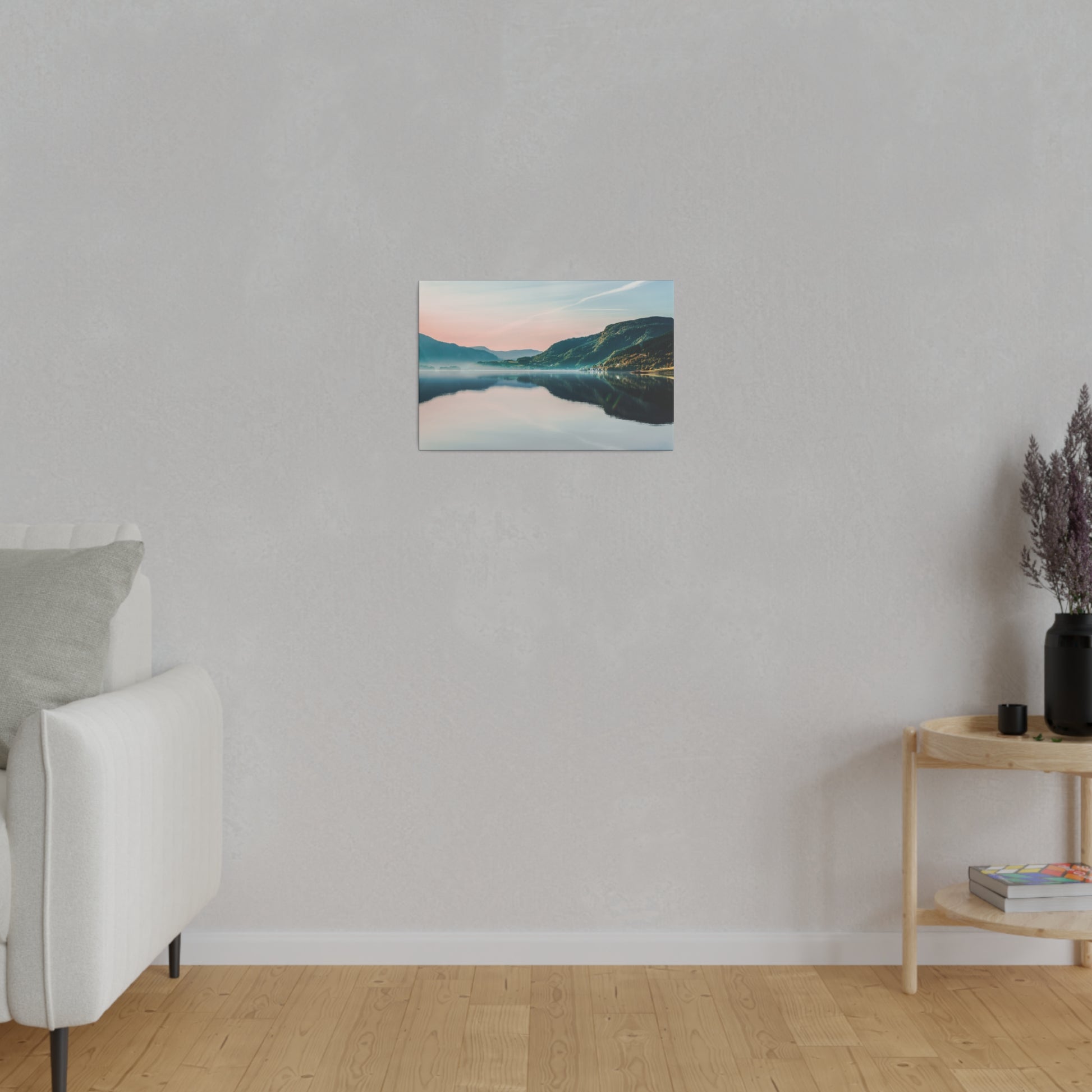 Small landscape photograph of a calm lake and mountains, mounted on a gray wall above a light wood floor.