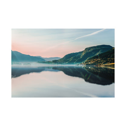 Panoramic lakeside landscape with calm lake reflecting pink sunrise and green mountains.