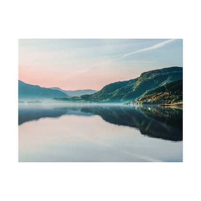 Calm lake with glassy water reflecting green mountains and a pastel pink-blue sky.