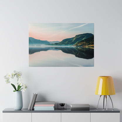 Landscape photograph of a calm lake reflecting mountains at sunrise, mounted on a white wall above a console with a yellow lamp.