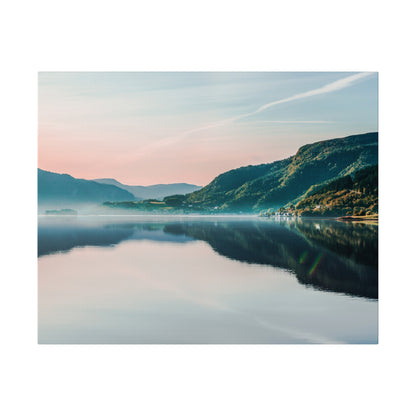 Wide view of a calm lake reflecting pastel pink and blue sky and green mountains across the water.