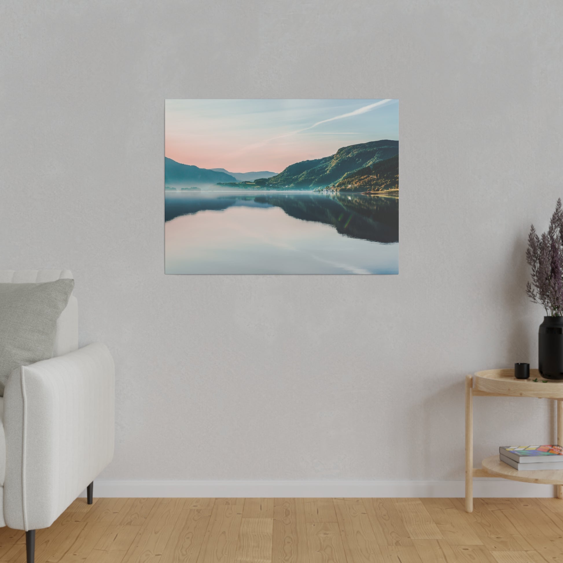 Framed landscape canvas of a calm lake reflecting mountains at sunset in pink and blue hues, hung on a light gray wall in a minimalist