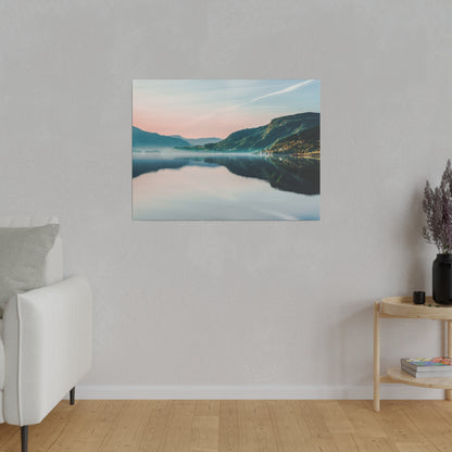 Framed landscape canvas of a calm lake reflecting mountains at sunset in pink and blue hues, hung on a light gray wall in a minimalist