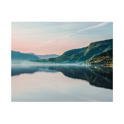 Calm lake at dawn reflects pink and blue sky and the green mountain range, with mist along the water.