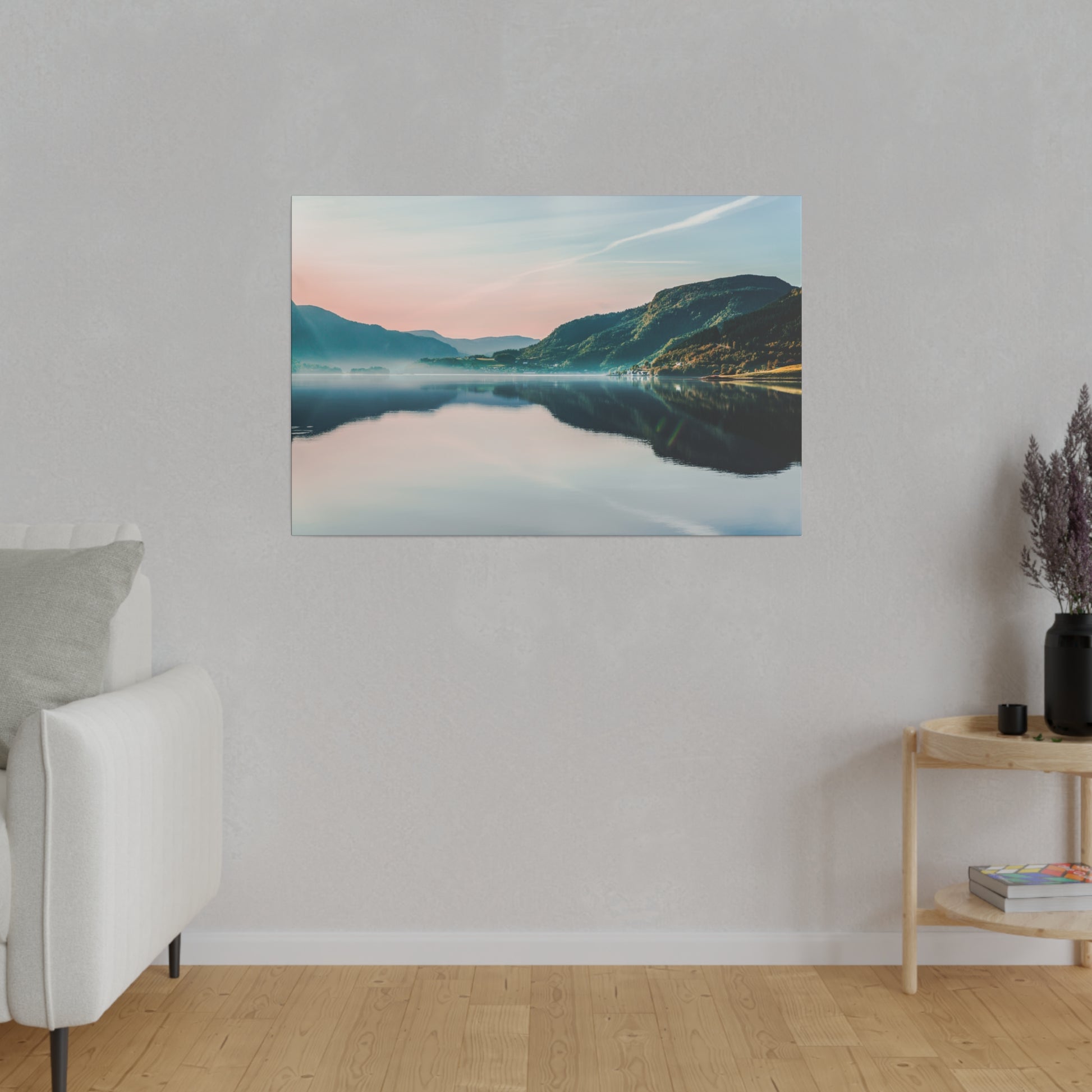 Canvas landscape print of a calm lake reflecting pastel sky and mountains, hung on a light gray wall in a minimalist living room.
