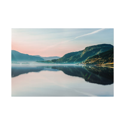 Wide panorama of a tranquil lake reflecting green mountains and pastel sky at dawn.