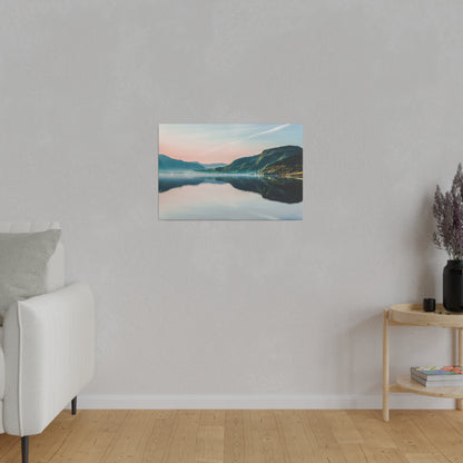 Framed landscape canvas of a calm lake and green mountains hung on a light gray wall, with a beige sofa and wooden side table nearby.