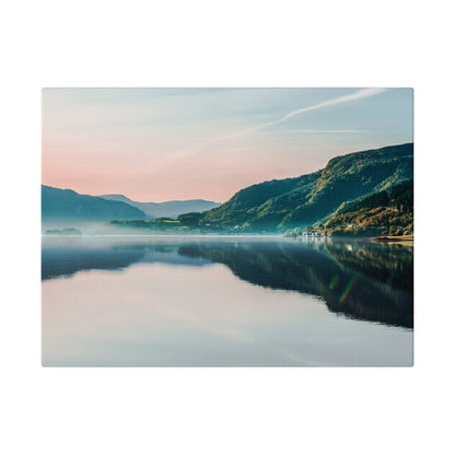 Calm lake reflecting pink and blue sky, with green mountains along the shoreline.