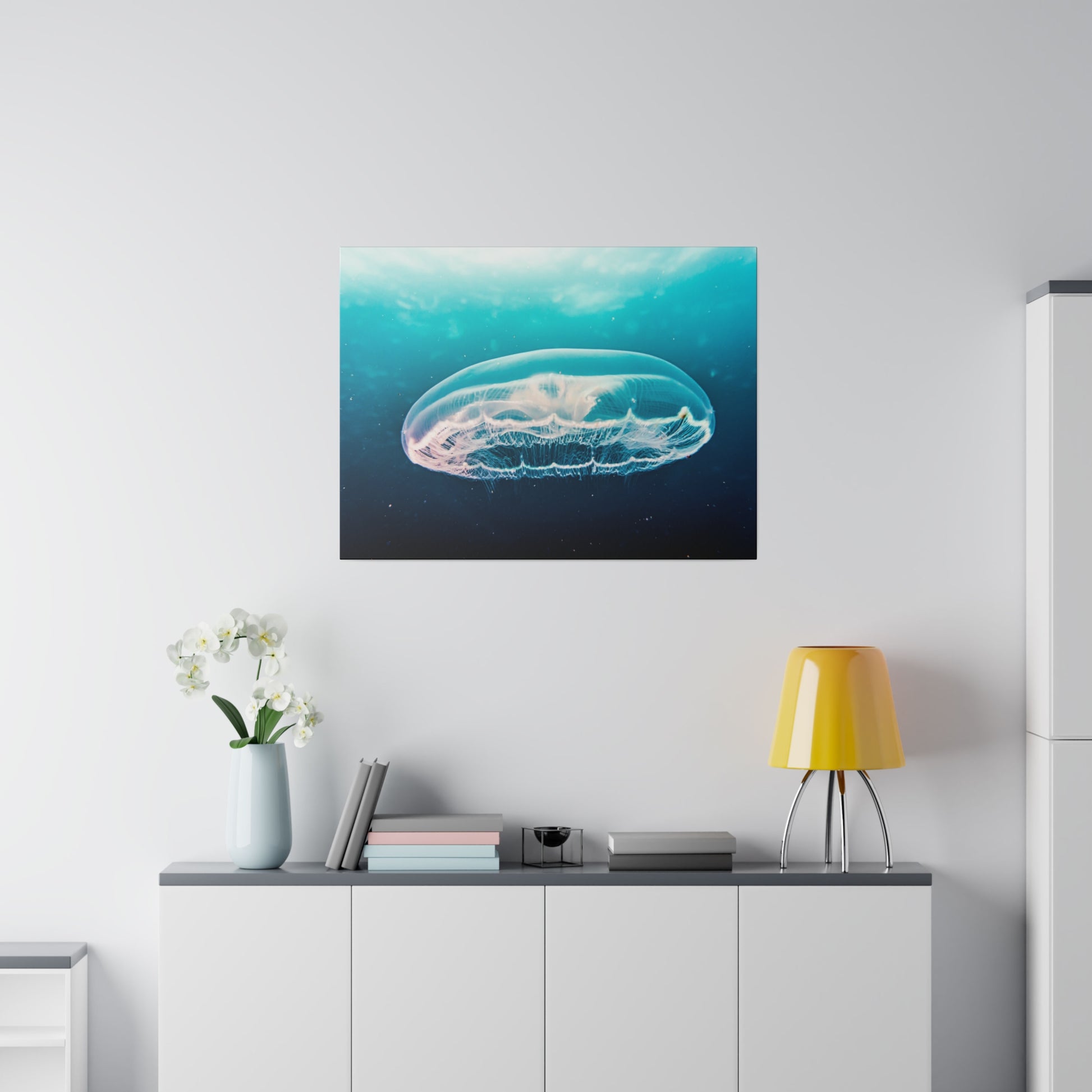 Framed underwater photograph of a translucent jellyfish in blue water hangs above a white sideboard in a bright room.