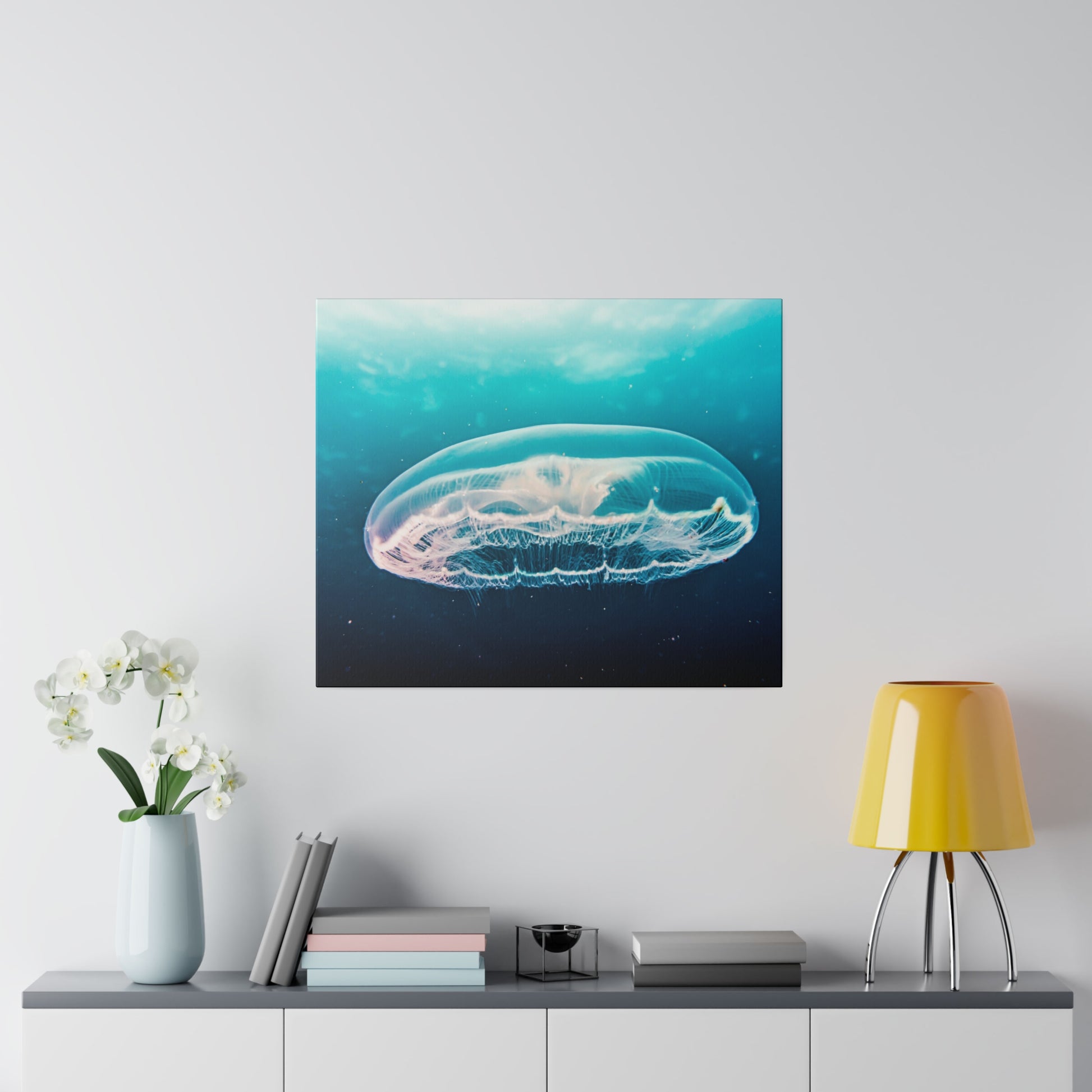 Square wall art depicting a translucent jellyfish in blue ocean water, mounted above a sideboard.