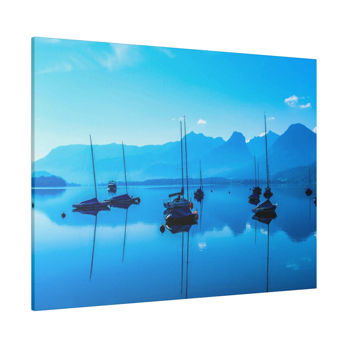 A serene lake at dawn, with sailboats anchored and the still water reflecting the blue sky. The mountains in the background add to the peaceful scene.