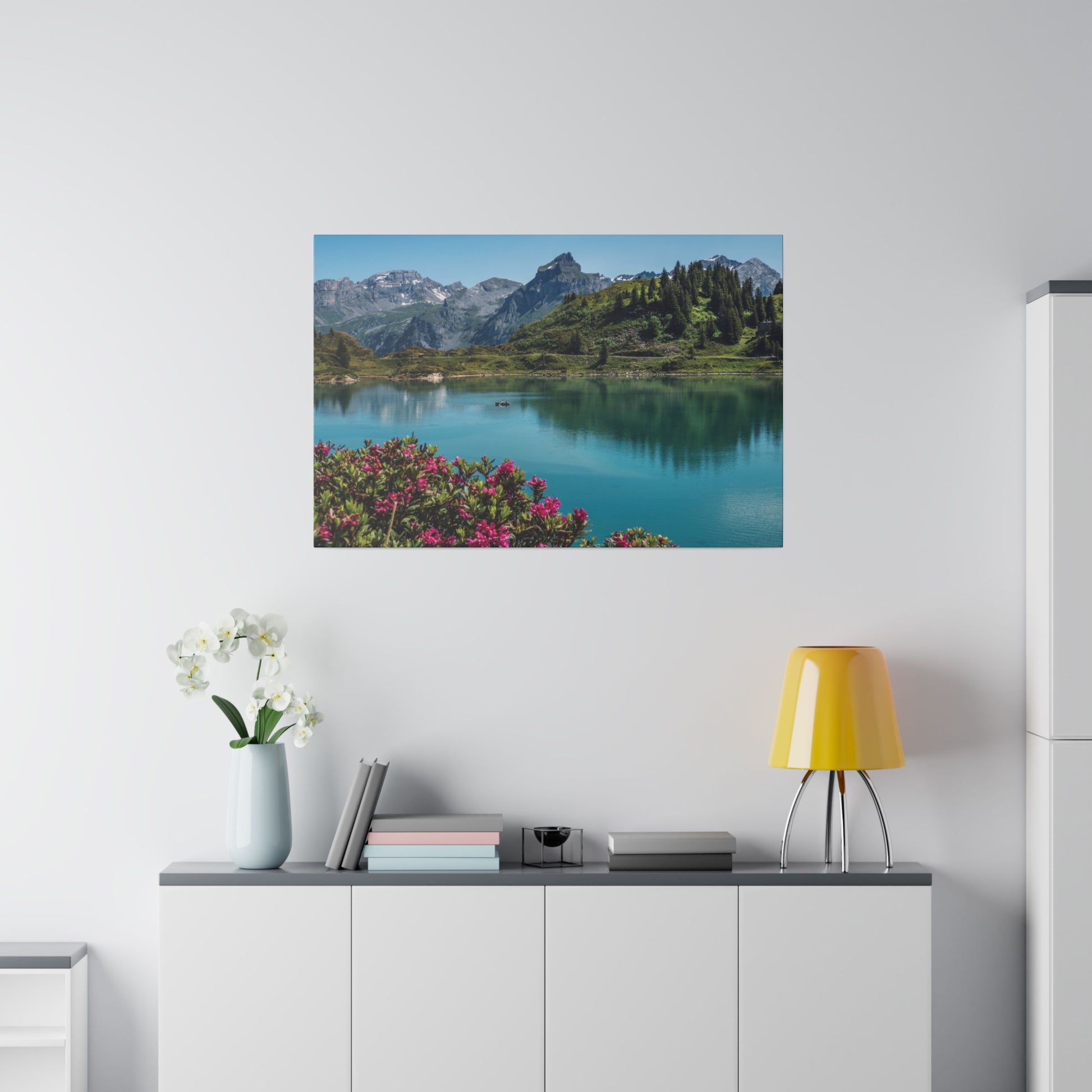 Wall-mounted landscape photograph of a turquoise lake with mountains and pink flowers in the foreground.