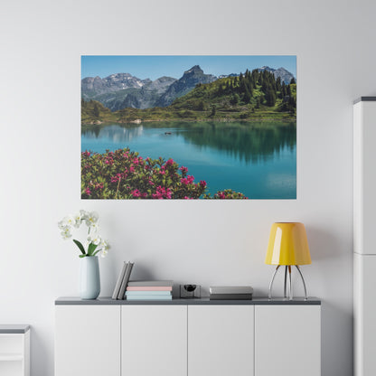 Mounted landscape wall art depicting a blue alpine lake with mountains and pink flowers in the foreground.