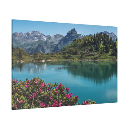 Turquoise alpine lake with green hills and snow-capped mountains in the background, and pink flowers in the foreground.