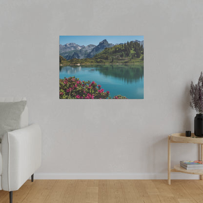 Photograph of a mountain lake with blue water, green hills, and pink flowers in the foreground, hung on a gray living room wall.
