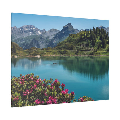 Turquoise alpine lake with pink flowering bushes in the foreground, a small boat on the water, and snow-capped mountains under a clear
