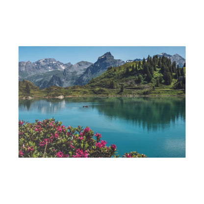 Alpine lake with turquoise water, surrounded by green hills, pine trees, and pink flowering shrubs in the foreground.