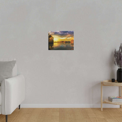 Small rectangular painting of a sunset over a river with trees, hung on a light gray wall in a minimalist living room.