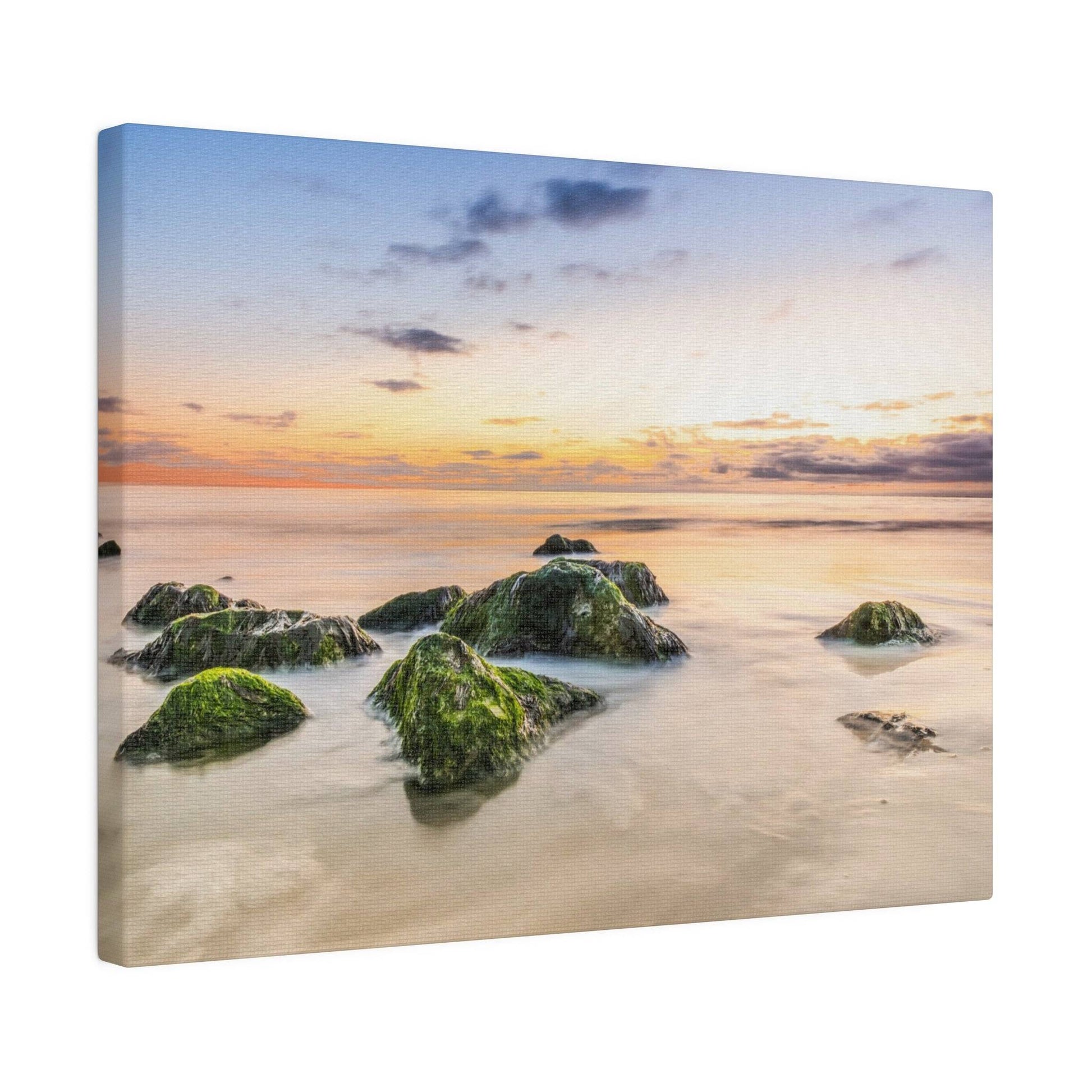 A seascape with green moss-covered rocks protruding from calm water at sunset.