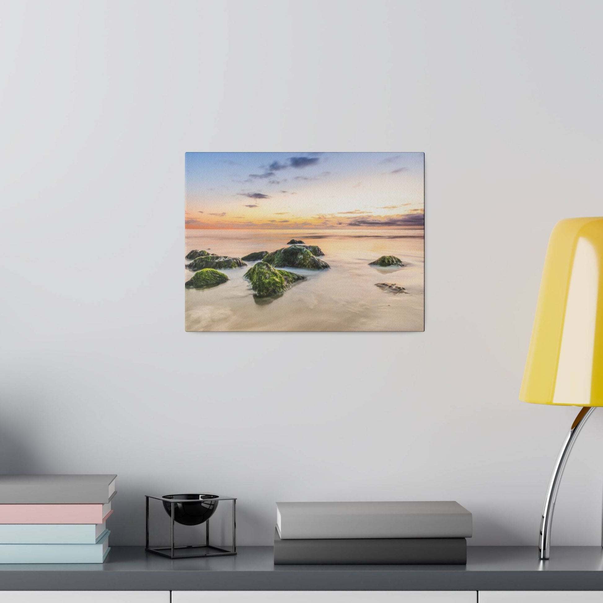 Canvas print depicting a sunset over a calm sea with moss-covered rocks in the foreground.