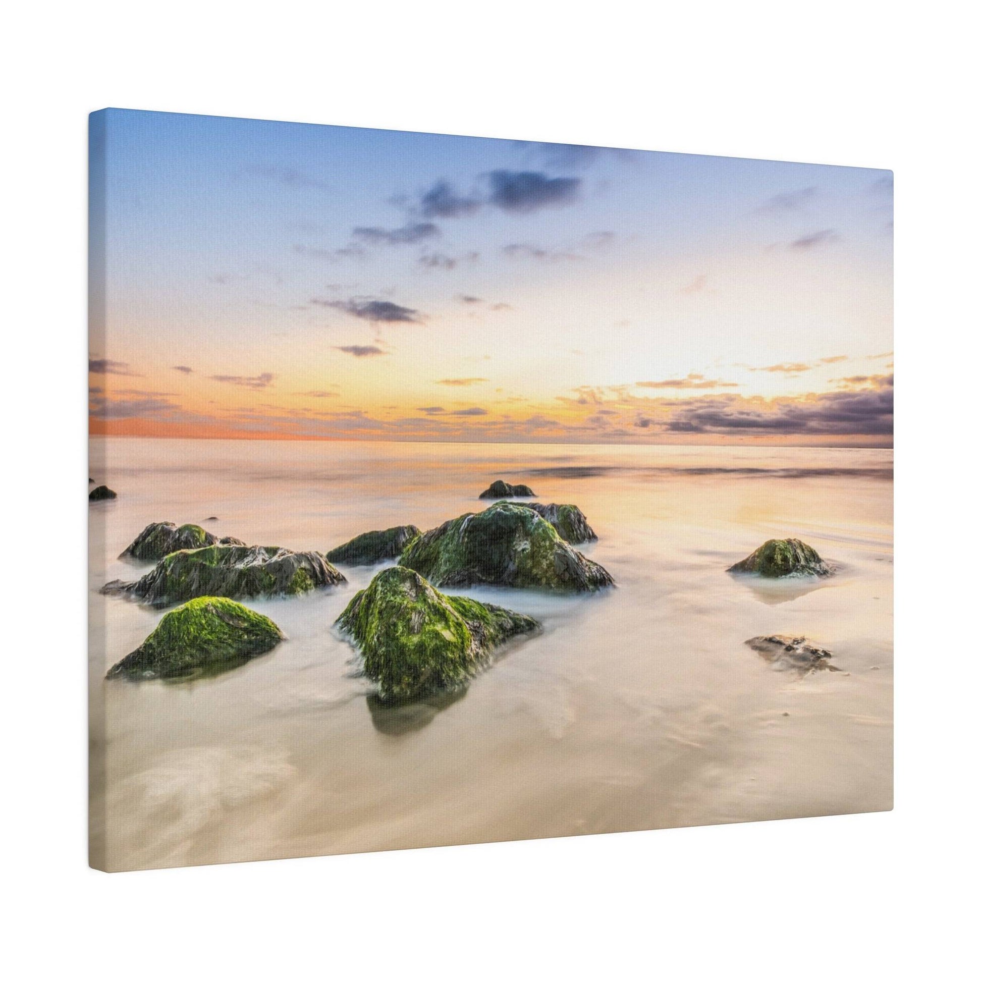 Photograph of moss-covered rocks in shallow ocean water at sunset, with a orange-to-blue sky.