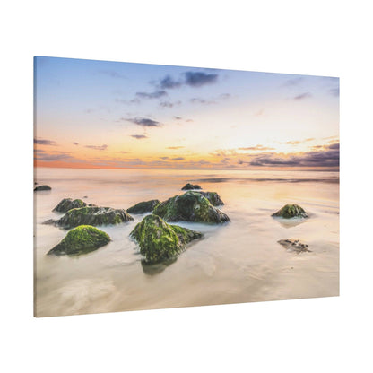 A canvas print of a seascape with moss-covered rocks in shallow water at sunset, featuring a pastel orange-to-blue sky.
